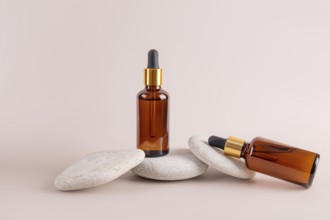 Two amber dropper bottles are artistically arranged on stacked smooth stones against a subtle beige