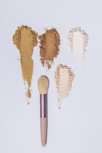 Top view of three different shades of face powder scattered artistically next to a makeup brush on