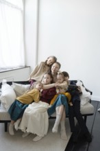 A large family sits together on a sofa in a cozy, bright living room They appear relaxed and