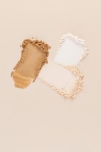 Top view of a split representation of compact and loose face powders, spilled on a beige background