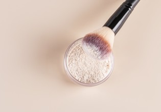 Top view of a makeup brush with pink and white bristles partially dipped into loose face powder,
