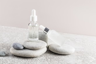 Two glass dropper bottles with clear and frosted finishes are placed elegantly on a stack of