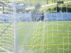 Close-up of a soccer goal net with a focus on the grid pattern under bright sunlight. Blurred green