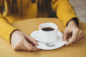 A cozy scene of a woman holding a cup of coffee on a wooden table She wears a warm yellow sweater,