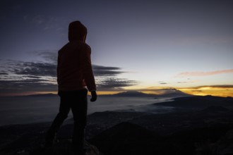 Back view of unrecognizable man standing at the summit during sunrise, overlooking distant