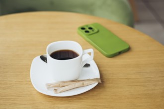 A cozy scene featuring a cup of coffee on a wooden table with a smartphone in a green case The