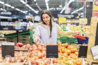 Woman in a casual hoodie shopping for fresh tomatoes in a vibrant supermarket, carefully choosing