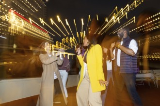 A group of friends joyfully dances and sings at a lively night party under city lights The