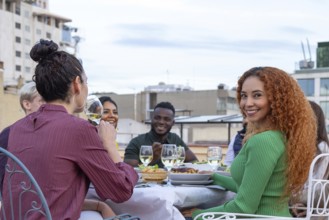 A group of friends enjoying a rooftop party, sharing drinks, food, and laughter under a clear sky