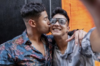 Latin gay couple taking selfie while embracing warmly. One partner kisses the other's cheek, while