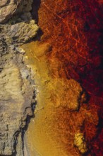 Striking aerial view of the Riotinto River, capturing its vibrant red and orange hues meeting rocky