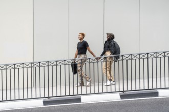 Two people walk hand in hand, smiling outdoors, expressing love and unity as a multiethnic couple.