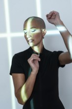 A middle-aged woman with a shaved head poses gracefully under artistic light patterns, radiating