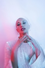 Middle-aged woman with shaved head in stylish pose, adorned with intricate attire. Artistic