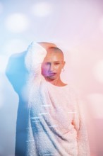 Middle-aged woman with shaved head poses confidently in creative lighting. The colorful bokeh
