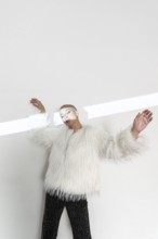 A middle-aged woman with a shaved head poses confidently in a luxurious white fur coat. The