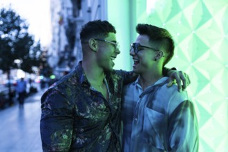 Latin gay couple enjoying an evening in the city, sharing laughter and embracing under vibrant neon