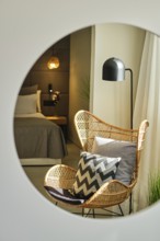 The elegant hotel room features a wicker chair with patterned cushions, a contemporary lamp and