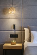 Elegant hotel room features a woven pendant light, modern upholstered wall, sleek bedside table