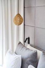 A cozy hotel room with a woven pendant lamp, plush gray pillows, and a textured gray upholstered