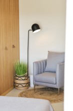 A cozy hotel room corner featuring a gray armchair, woven basket with green plant, and a sleek