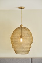 A stylish woven pendant light hangs from a hotel room ceiling, casting a warm glow. The beige color