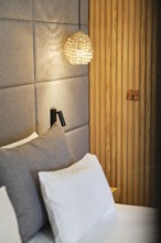 A modern hotel room features soft gray bedding, ambient pendant light, and vertical wood accents,