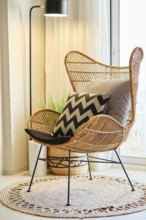 A cozy hotel room features a stylish wicker chair adorned with chevron-patterned and plain cushions