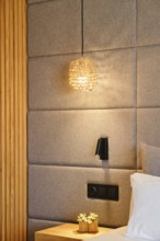 A serene hotel room with soft, woven pendant lighting, padded walls, and wooden accents, creating a
