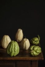 A rustic display of fresh chayote on a dark wooden table against a black background. The vegetable