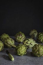 Fresh artichokes arranged artfully on a dark, textured surface, ideal for culinary and healthy