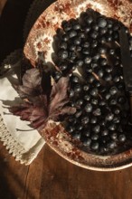 A rustic autumn still life featuring fresh blueberries on a vintage decorative plate. A dry maple