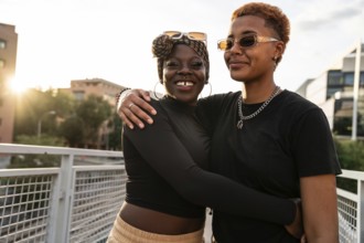 An LGBT multiethnic couple embraces warmly on a pedestrian bridge. They smile with genuine