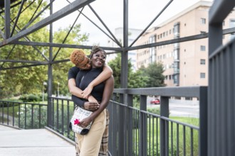 An affectionate LGBT multiethnic couple embraces on a city bridge, radiating happiness and love.