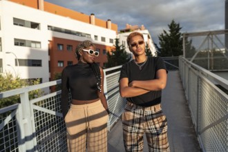 A stylish LGBT multiethnic couple poses confidently on an urban bridge under the warm, golden