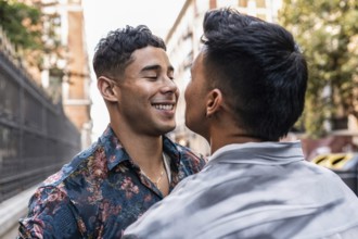 A smiling latin gay couple enjoys a romantic moment on a sunny day in Madrid. They are embracing,