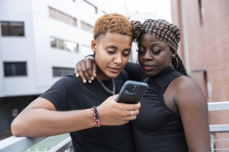 A loving multiethnic couple stands close, sharing a moment while looking at a smartphone. They