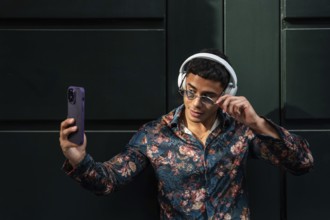 A trendy latin man in floral shirt and sunglasses takes a selfie outdoors, showcasing modern style