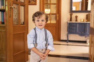 A young boy stands confidently dressed in a light blue shirt with suspenders. He is in an elegantly