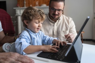 A young child types on a tablet keyboard, guided by an adult. They are sitting together at a table