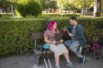 A couple sits on a park bench studying The woman, with vibrant pink hair, uses crutches due to her