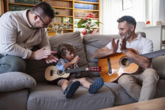A loving gay couple enjoys quality time with their young son, playing guitars in the cozy living