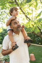 A cheerful father and his young son enjoy a sunny day in the garden. The father carries the child