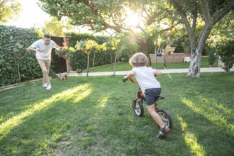 A cheerful scene of a father playing with his young son learning to ride a bicycle in a sunlit