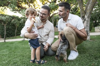 A joyful family moment in a lush garden with a gay couple watching their son eating a banana, and a