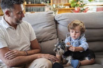 A child explores the role of a vet, using a stethoscope on a small dog, with a smiling father
