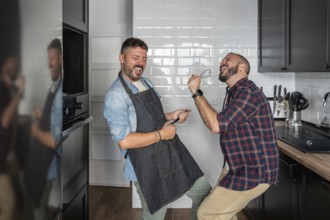 A cheerful gay couple enjoys a playful moment in their modern kitchen, passionately dancing and