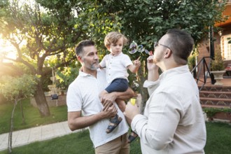 A joyful gay couple spends a sunny afternoon outdoors with their young son, engaging in playful