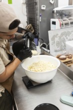 A baker at an Italian bakery carefully pours white chocolate chips into a bowl to weigh it The