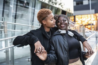 A joyful LGBT multiethnic couple shares a tender moment outdoors. They hold hands and smile warmly,